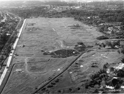 An aerial shot of RNWS Kranji - This is taken from a northerly direction looking south.
This is taken from a northerly direction looking south. It shows the old aerial field which my father believes was built originally as an oil container field before the war. In 1941 the oil containers were all set on fire during the Japanese invasion. The aerials are radio aerials that served WRNS Kranji. The straight road visible left was "Woodlands Road" which ran along the railway line. In between is the monsoon drain.2/3rds up the road is the entrance to the level crossing where there was the hut which was lived in by the keeper. The village to the left of the railway line was Yew Tee village, where my amah lived in a kampong.

The bungalow visible bottom left was lived in (1970-2) by Cdr Baller. The roof visible next to it is of bungalow 7 where we lived for the first 2 months of our time in Singapore before moving up the hill to the base which can be seen top right of the picture. the tall microwave aerial is visible in front of the white cliffs of the quarry on the horizon.

My father remembers the wealthy labour contractor Koonho who had the grass cutting contract for all the naval bases. This huge aerial field had approximately 100-200 men working in lines with long-handled scythes trying to keep the vegetation down.
Keywords: Lucy Childs;RNWS Kranji;Woodlands Road;Cdr Baller;Koonho