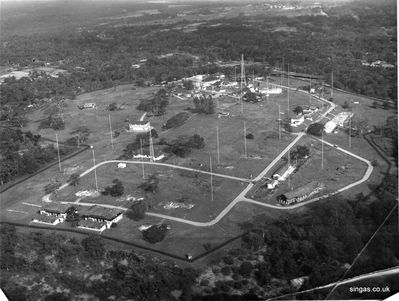 An aerial shot of RNWS Kranji from the south east (approx)
An aerial shot of RNWS Kranji from the south east (approx) showing the full expanse of the hill top station. The two storey building to the centre left of the photo was the Signal Training Centre (STC) which in my Dad's time was run by Sub Lt. Singleton who trained any signalmen who came up from the fleet. The station was a communications training base for many passing servicemen.

 The two buildings to the south of the rectangle road were 2 remaining barracks (the foundations of former barracks can be seen around the rectangle. Opposite those barracks are 2 bungalows lived in by CPOs Warmsley and Maddox.

 In the trapezium shaped road to the right is a long white bungalow which was the police quarters and the green area within the trapezium shaped road is where they held the Muniandi festival.

The straight road leading north from that area goes past the cinema on the left and several storage buildings including the diesel storage unit. The road then bends round to the left past the Popperwell's  house on the right. It then passes behind the main buildings of the station. You can just see the east facing wall of our bungalow before the road disappears behind the microwave tower. From that road you could look out over the aerial field to the northeast. I believe this is now where the Singapore army Signal School is. I think  Kranji Expressway now runs beneath this point in the valley between the former aerial field  and the hill rising to the station.
Keywords: Lucy Childs;RNWS Kranji;Sub Lt. Singleton;signalmen;Warmsley;Maddox;Popperwell